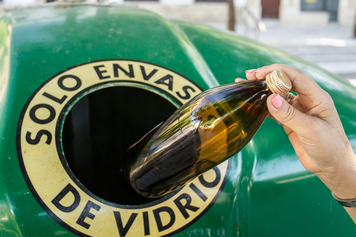 Una persona introduce una botella de vidrio en el contenedor verde para reciclar.  - MANU GARCÍA