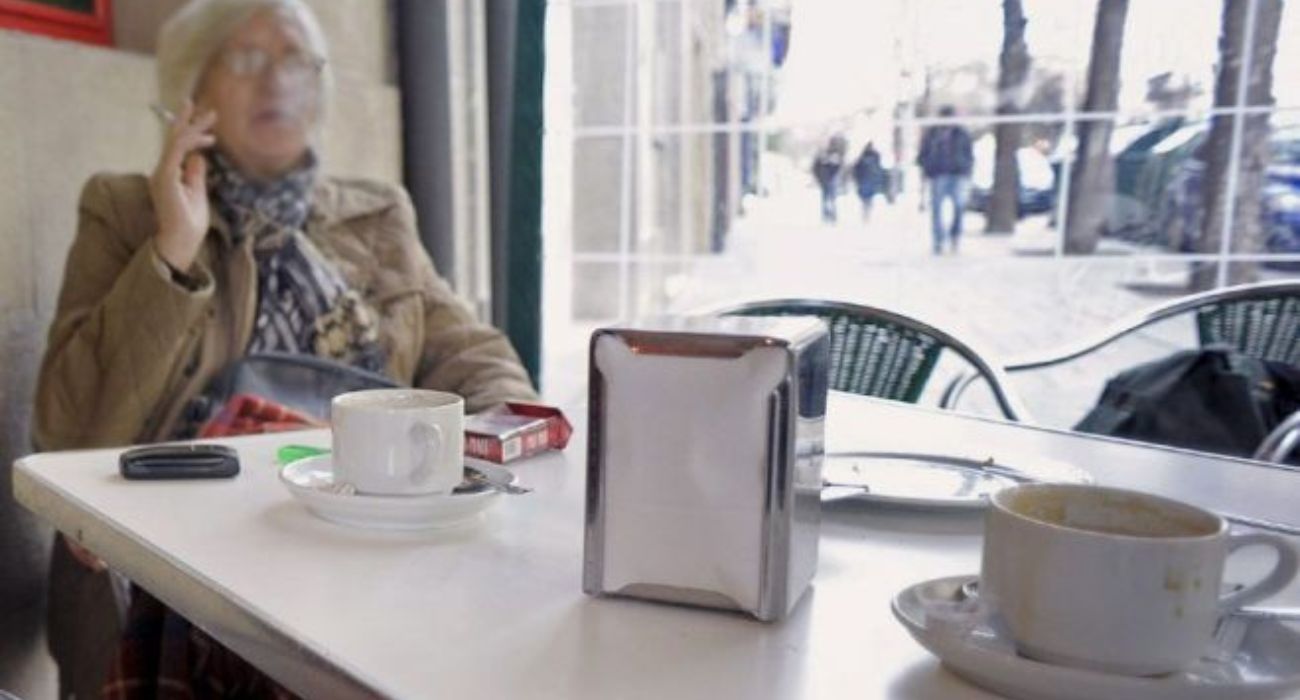 Una señora fuma mientras se toma un café en una terraza cerrada. - Una señora fuma mientras se toma un café en una terraza cerrada.