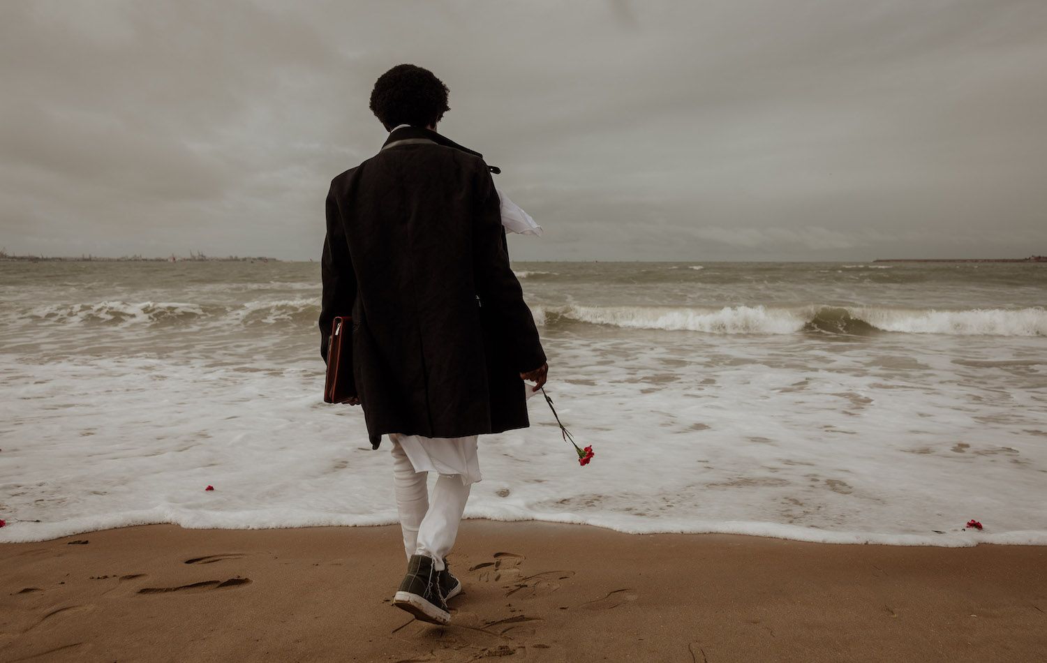 Un joven inmigrante se acerca al mar para arrojar una flor en recuerdo de las víctimas de la 'patera de Rota'.