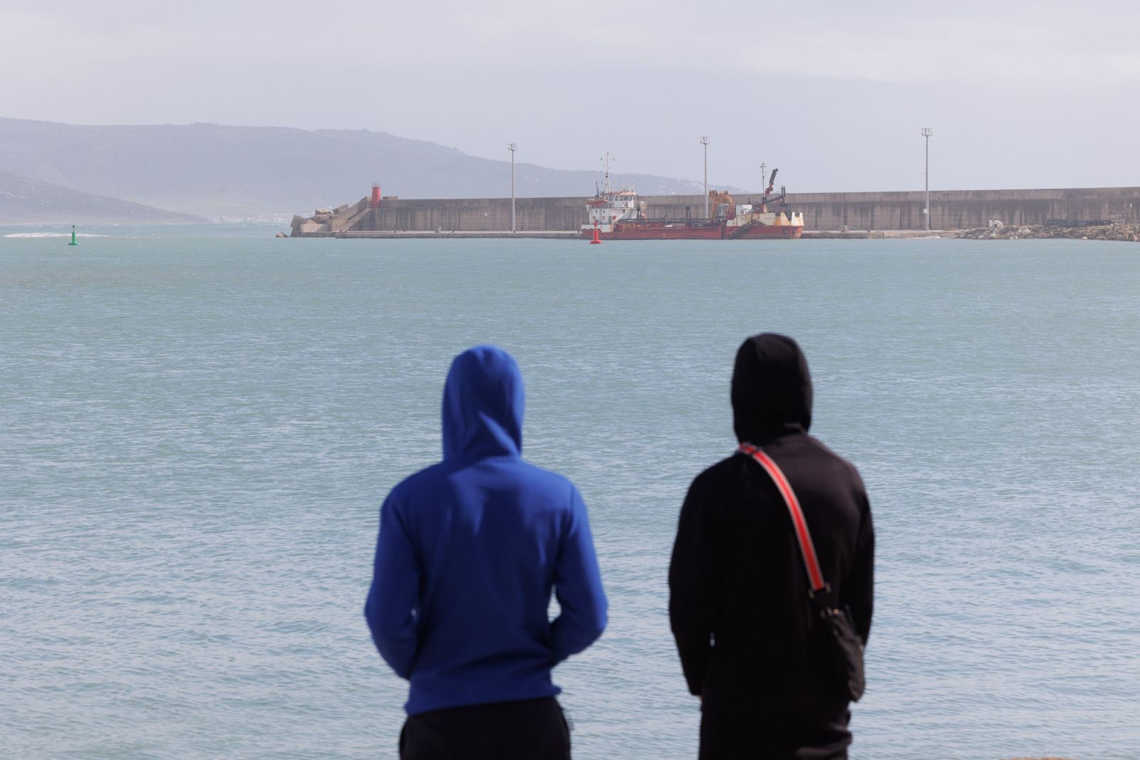Dos de los testigos del ataque mortal, al día siguiente en el puerto de Barbate, miran hacia el lugar de la tragedia.