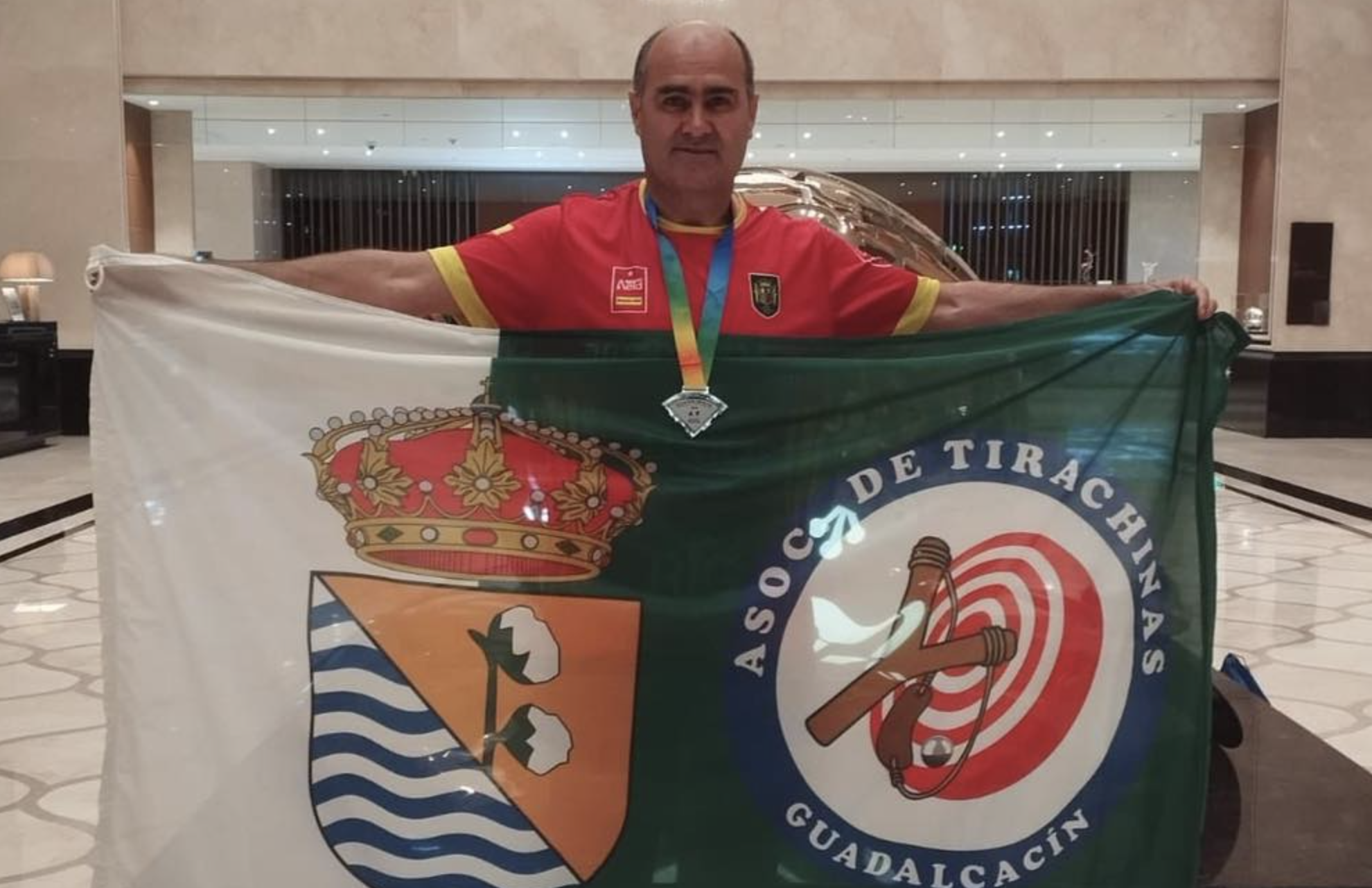 José Vela, en China, con una bandera con el escudo de Guadalcacín y de la Asociación de Tirachinas de esta ELA de Jerez. José Vela, en China, con una bandera con el escudo de Guadalcacín y de la Asociación de Tirachinas de esta ELA de Jerez.