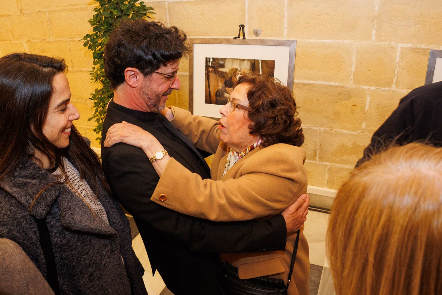 Emilio Morenatti se abraza a su madre, Rosa, en presencia de Marta, su mujer, tras el pleno extraordinario donde ha sido distinguido como Hijo Adoptivo de Jerez. Al fondo, una de las fotos de su exposición en los Claustros con sus trabajos de la pandemia por los que recibió el Pulitzer.
