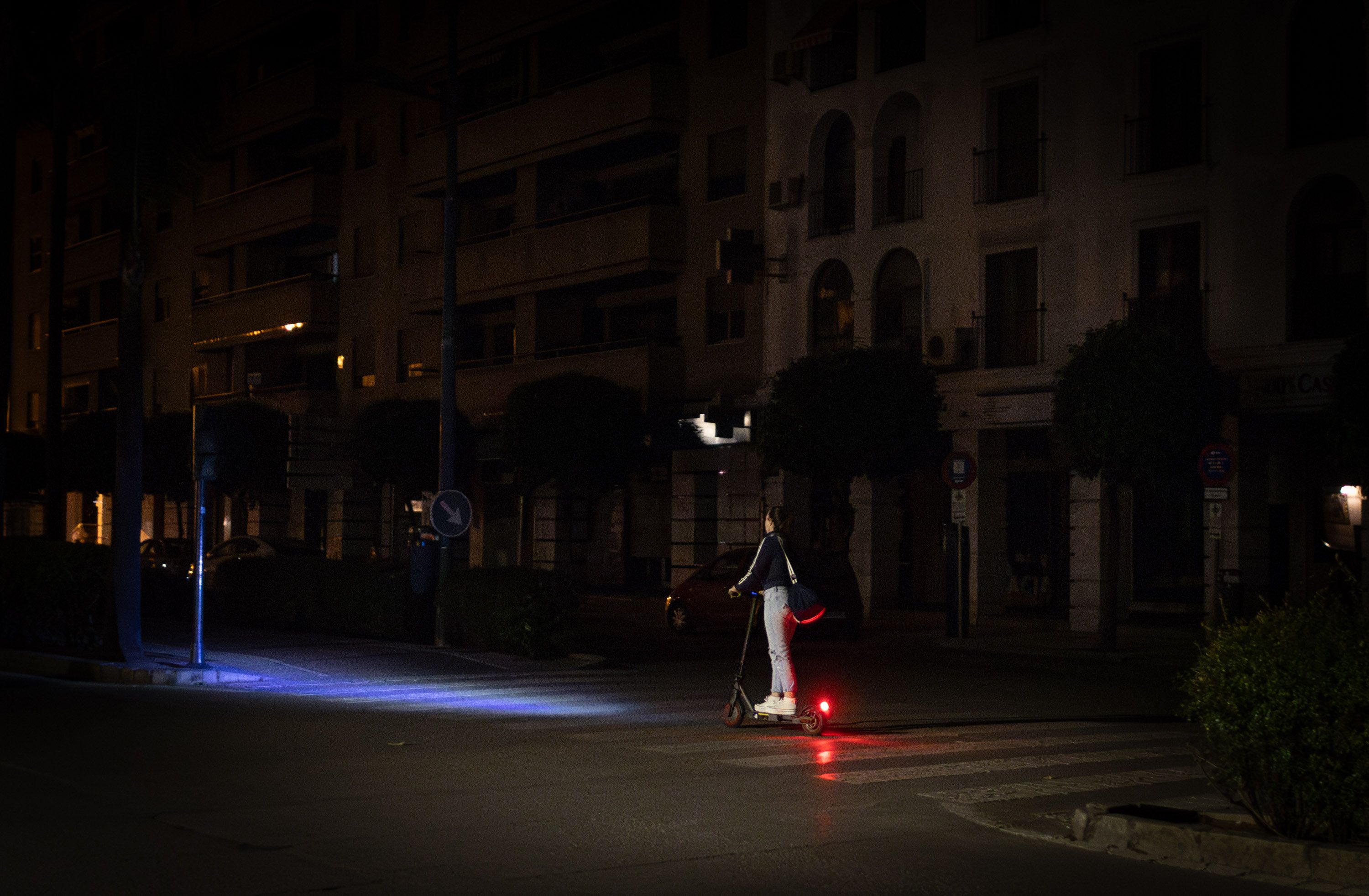 Un patinete circula por la Avenida Álvaro Domecq el lunes por la noche, aún sin luz, mientras al fondo algunas zonas ya tienen electricidad.
