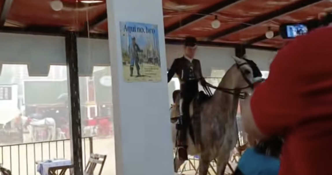 Un casetero deja entrar a un joven jinete en su caseta en mitad del diluvio en la Feria de Jerez.