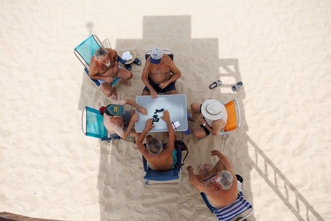 Varias personas jugando al dominó en la playa en Rota.