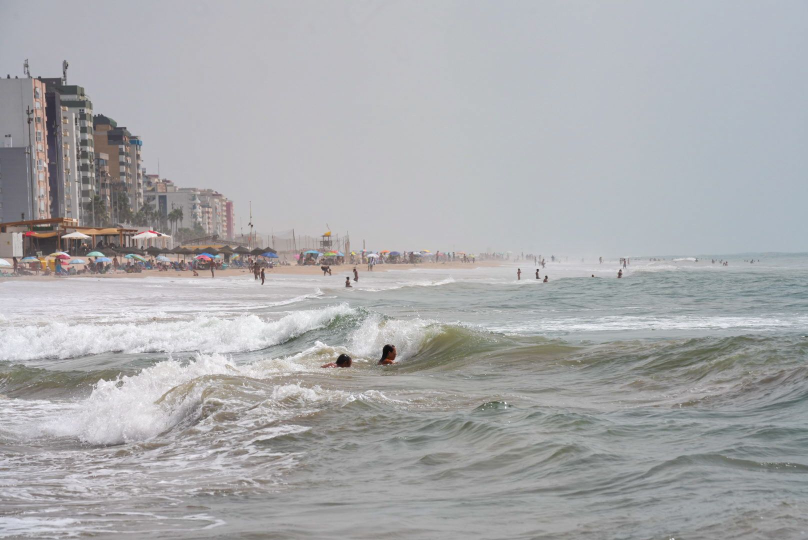 Personas bañándose en la playa en Cádiz con mar de fondo.