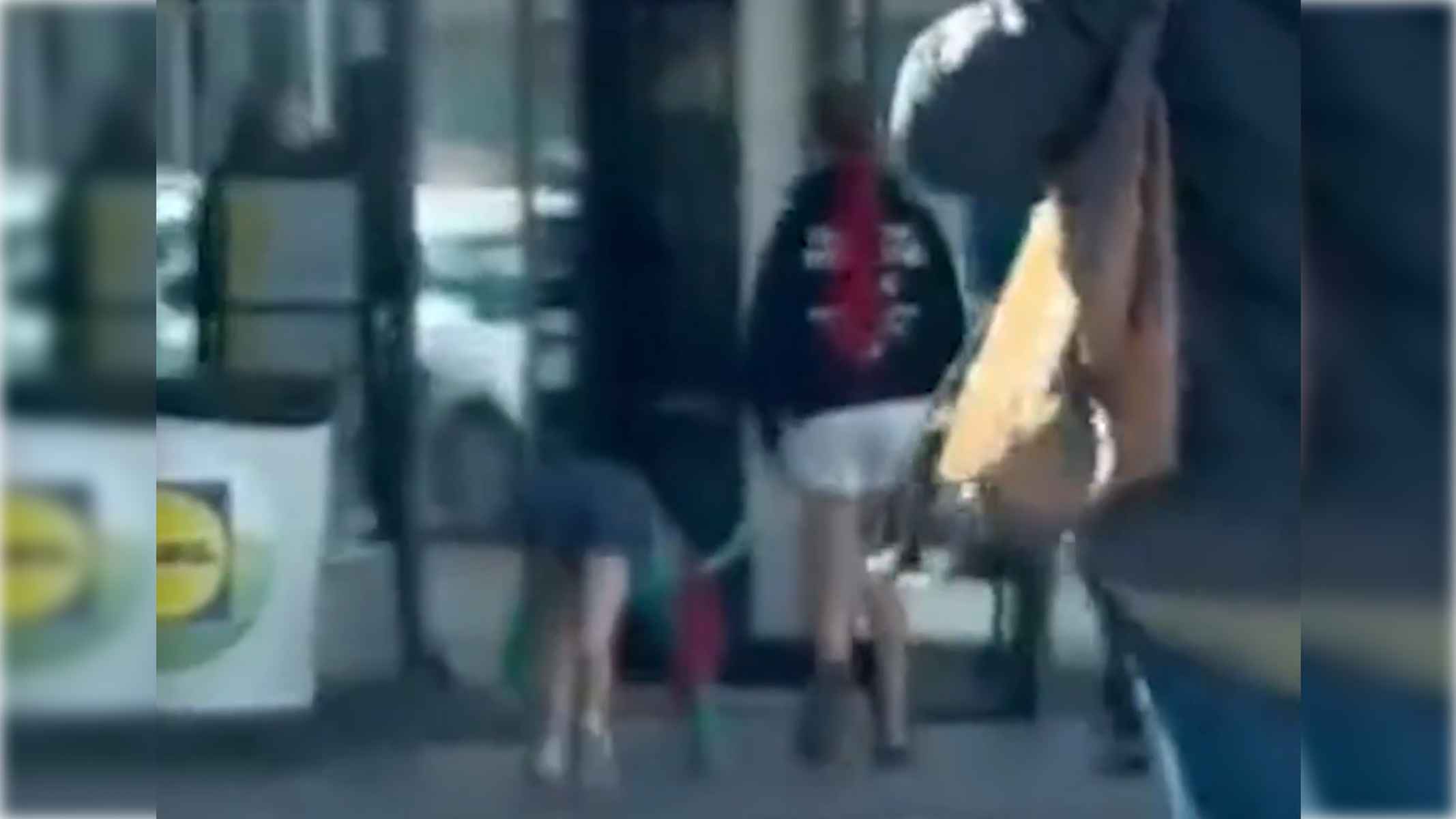 Una joven 'therian', caminando a cuatro patas y siendo paseada por otra joven a la entrada de un supermercado.