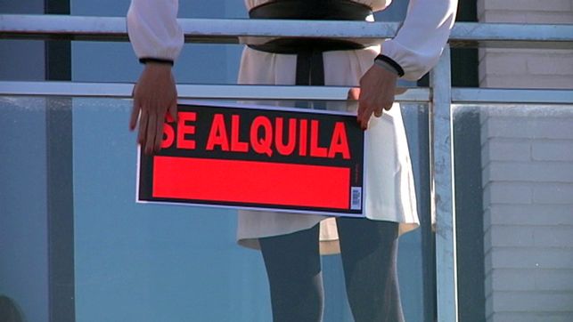 Una mujer colocando el cartel de alquiler.