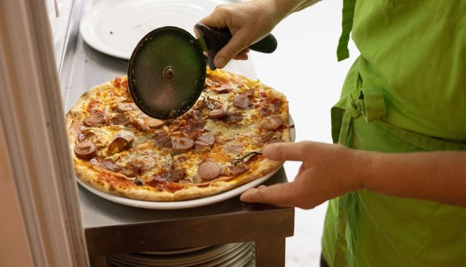 Joanna cortando una pizza en la cocina.