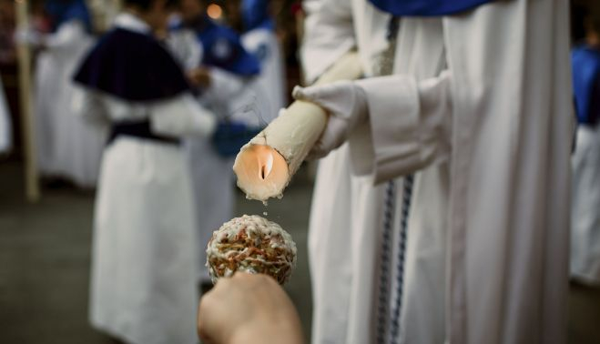Un nazareno de La Borriquita dando cera a un pequeño.   ESTEBAN